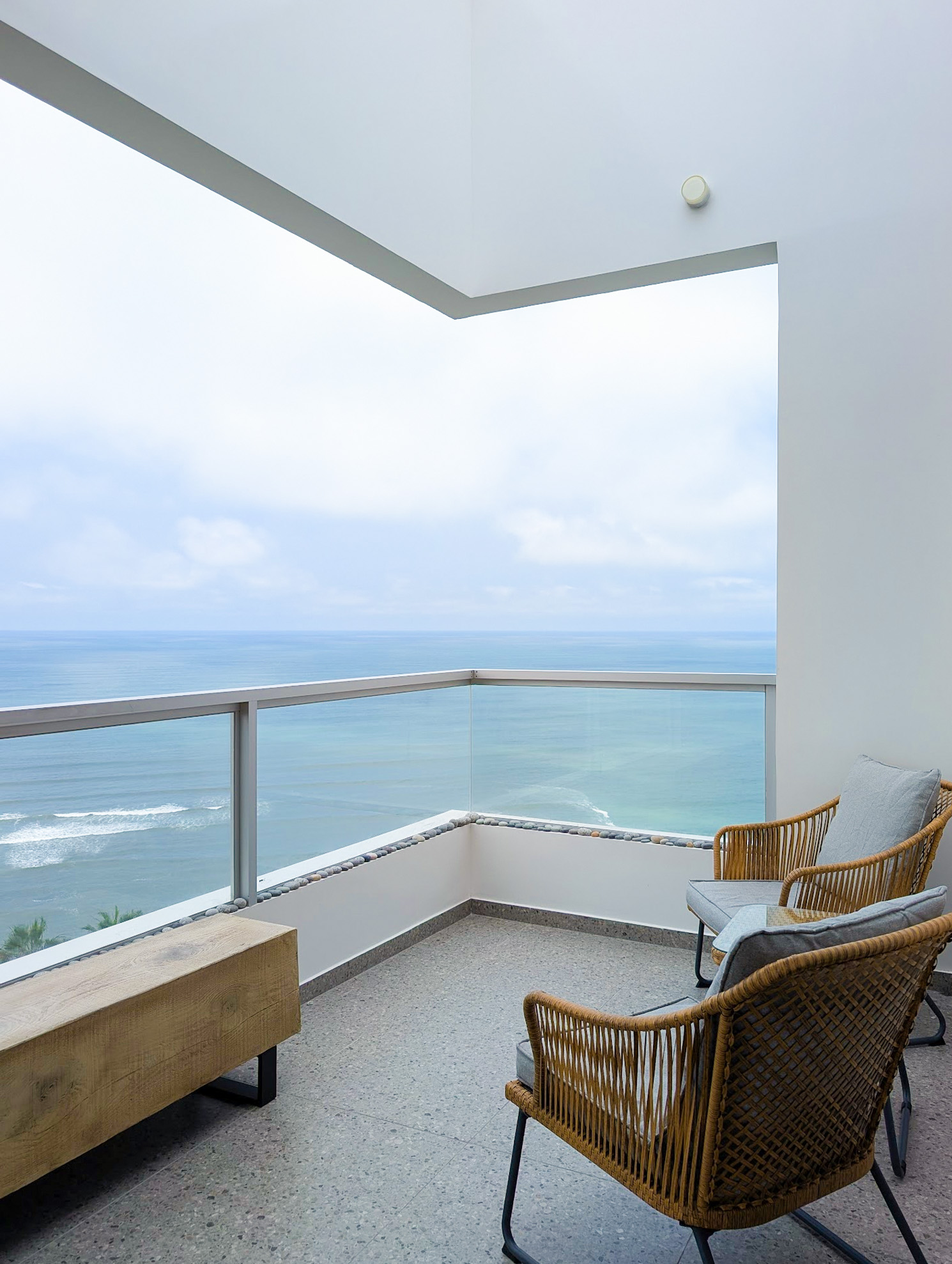 The private corner balcony at Vista Malecón, with glass railing, wicker seating, and an open view over the Pacific Ocean in Miraflores, Lima